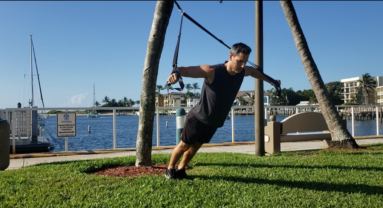 Athlete working out with the NOSSK TNT anchored from a palm tree trunk outside
