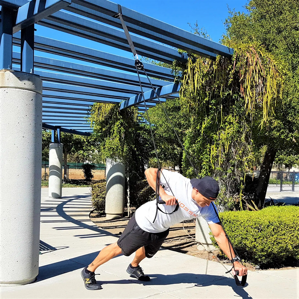 A man performing a suspended plank outdoors using the NOSSK Twin Pro Suspension Bodyweight Trainer